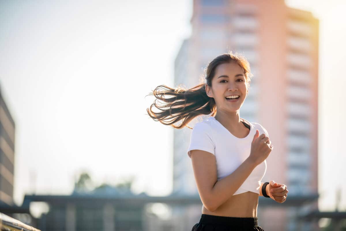 Woman in a ponytail and workout clothes running outside in the sunshine.