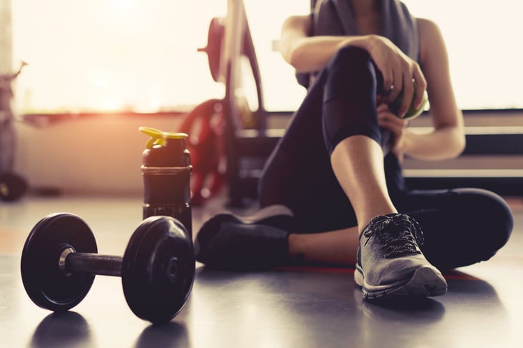 Woman sitting on the gym floor with dumbbell and water bottle.